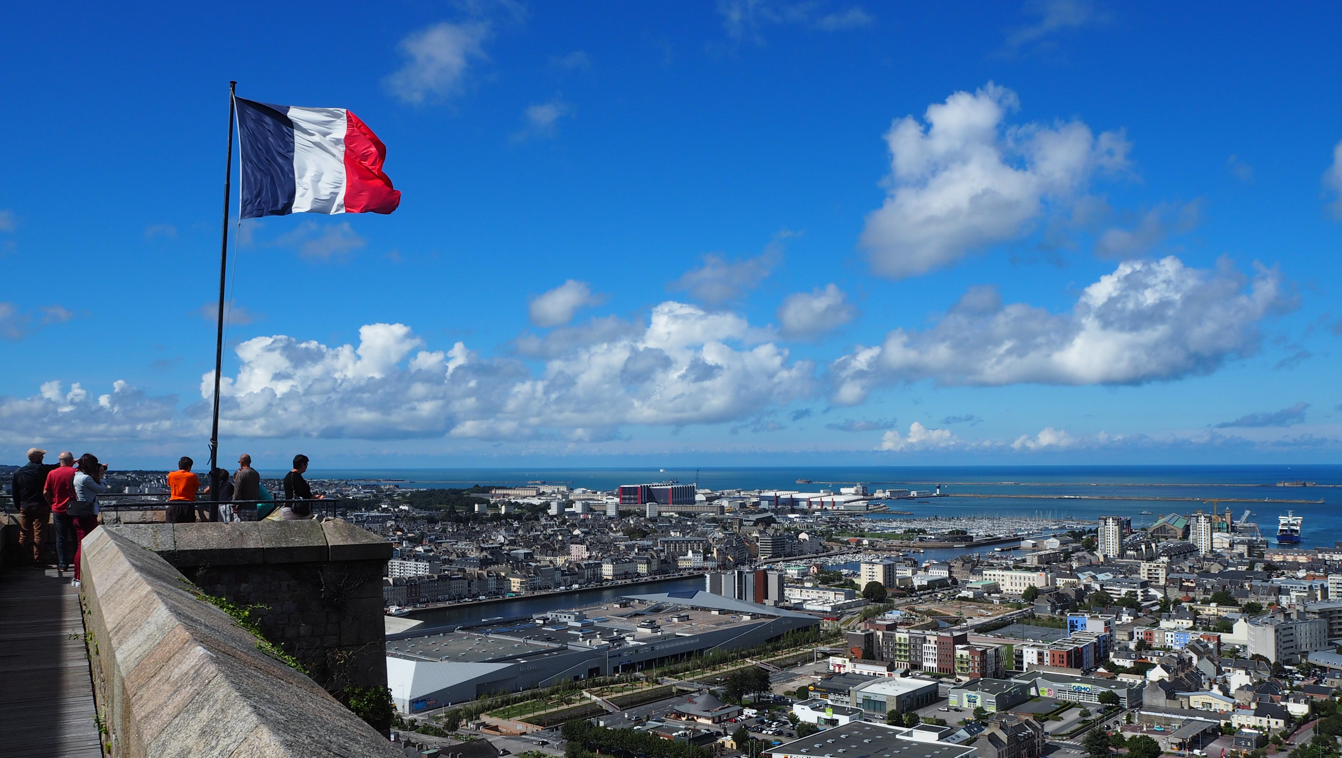 Flag of France against a blue sky above the city of Cherbourg.